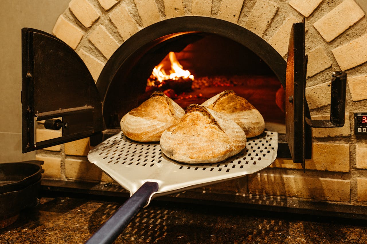 Three sourdough loaves bake in a rustic brick oven, showcasing traditional culinary craftsmanship.